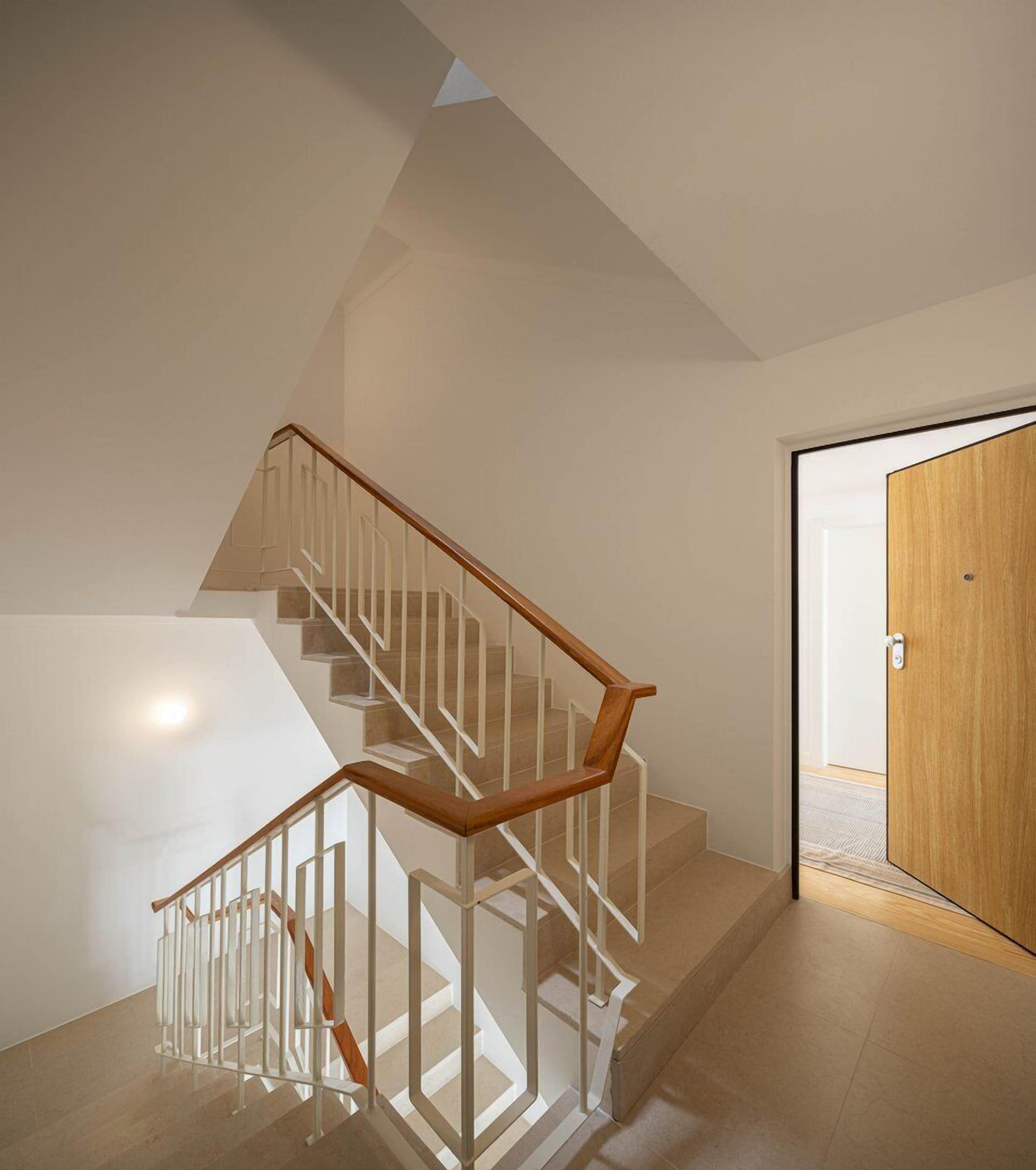 A modern staircase with glass railings and wooden steps, leading to a room with a wooden door.