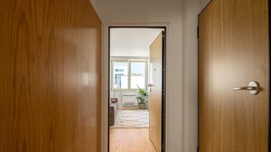 A hallway with wooden doors leading to a room with a window, a radiator, and a plant. - Azul Downtown Apartments - Sé Velha (Coimbra)