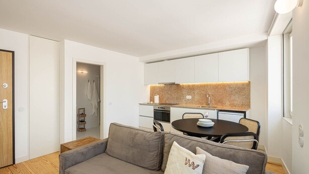 A modern apartment with a grey sofa, a dining table, and a kitchen area with white cabinets and a granite countertop. - Azul Downtown Apartments - Sé Velha (Coimbra)