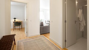 Un apartamento moderno con suelo de madera, un escritorio con silla, un sofá y un baño con una toalla colgada en la puerta.