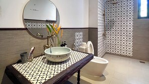 A bathroom with a round mirror, a sink with a patterned countertop, a toilet, and a shower area with patterned tiles.