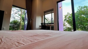 Een moderne hotelkamer met een groot bed, een bureau en een raam met uitzicht op groen.