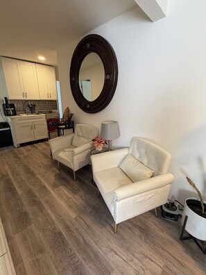 A modern living room with two white leather sofas, a round mirror, a lamp, and a potted plant.