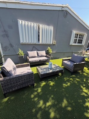 A covered outdoor seating area with wicker furniture and artificial grass.