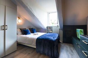 Un dormitorio moderno con cama, televisor, escritorio y ventana.