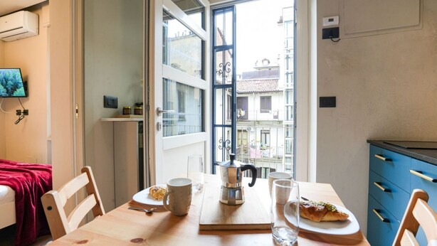 A cozy dining area with a wooden table, chairs, a coffee pot, and a pastry on a plate. - Torino Centro, Gioberti Suite (Torino)
