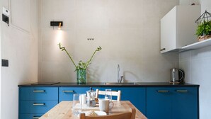 A modern kitchen with blue cabinets, a wooden table, and a vase with green plants. - Torino Centro, Gioberti Suite (Torino)