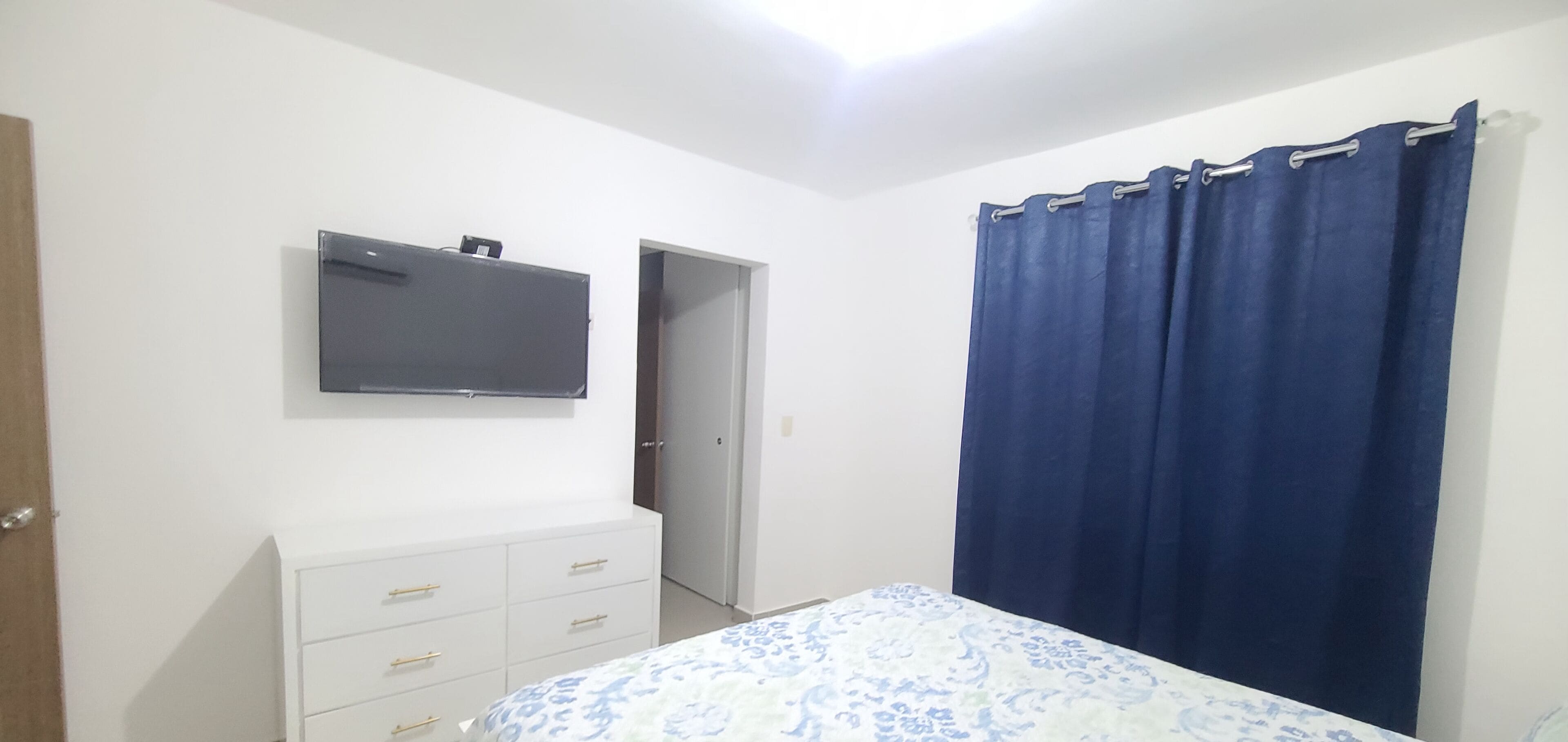 Une chambre à coucher avec un lit, une commode, un téléviseur et une porte.