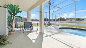 A covered outdoor area with a pool, chairs, and a table. - Spectacular Oasis + Pool + Games + Pet friendly (Kissimmee)