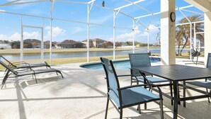 A covered outdoor area with a pool, lounge chairs, and a table. - Spectacular Oasis + Pool + Games + Pet friendly (Kissimmee)