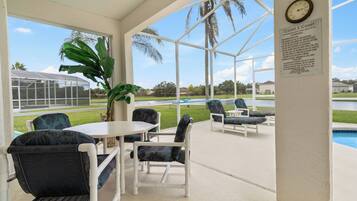 Relax in the covered outdoor seating area with a view of the swimming pool, perfect for dining or socializing.