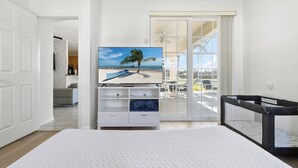 A bedroom with a bed, a TV on a dresser, a crib, and a view of the beach through a sliding door. - Spectacular Oasis + Pool + Games + Pet friendly (Kissimmee)
