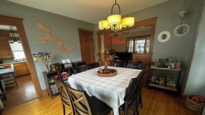 A dining area with a table set for four, surrounded by wooden chairs, a chandelier, and a wall-mounted mirror.