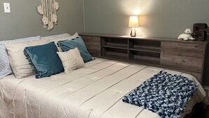 A bedroom with a bed, bedside table, lamp, and a dreamcatcher on the wall.