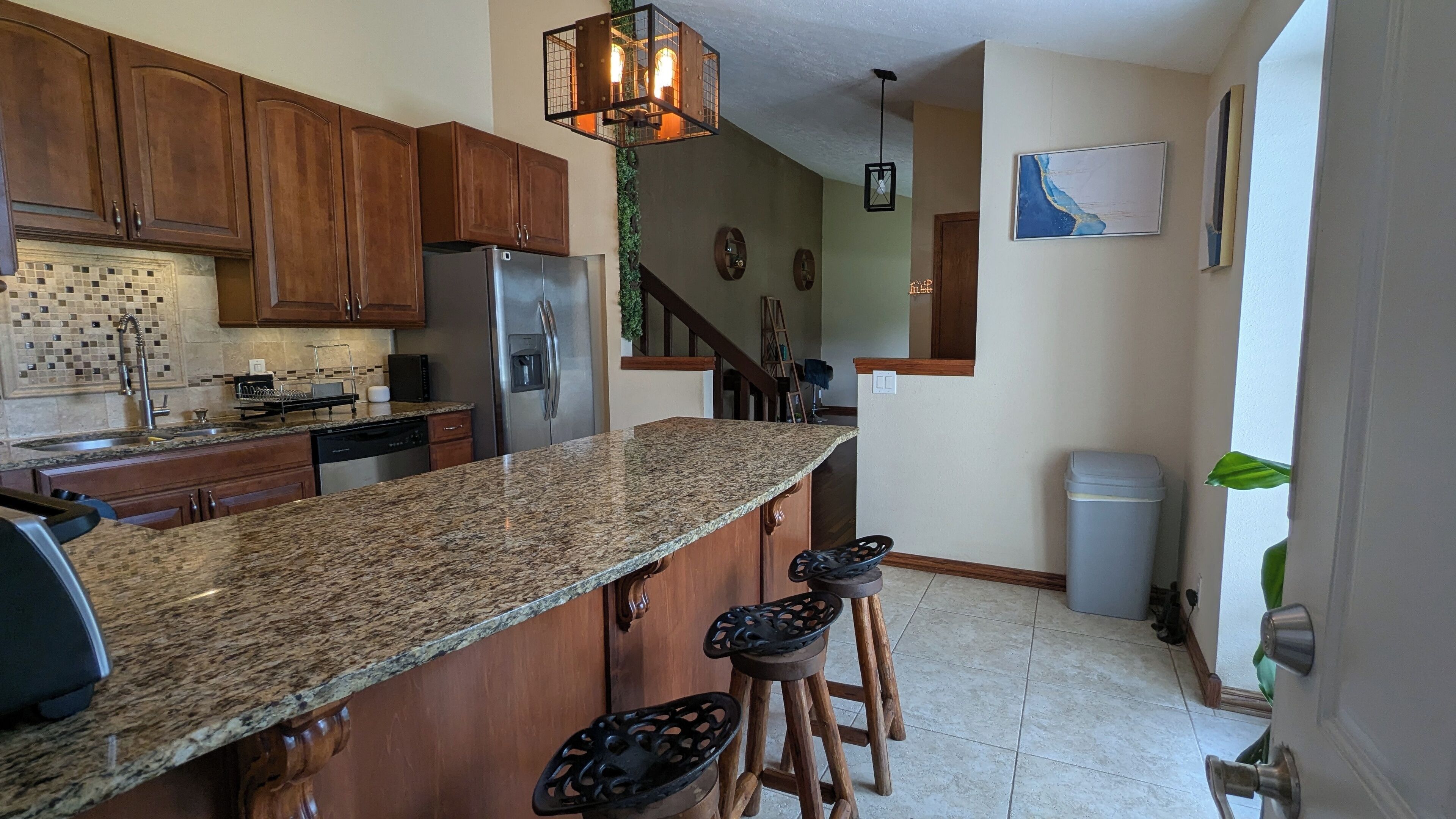 A kitchen with granite countertops, wooden cabinets, a stainless steel refrigerator, and a built-in island with bar stools.