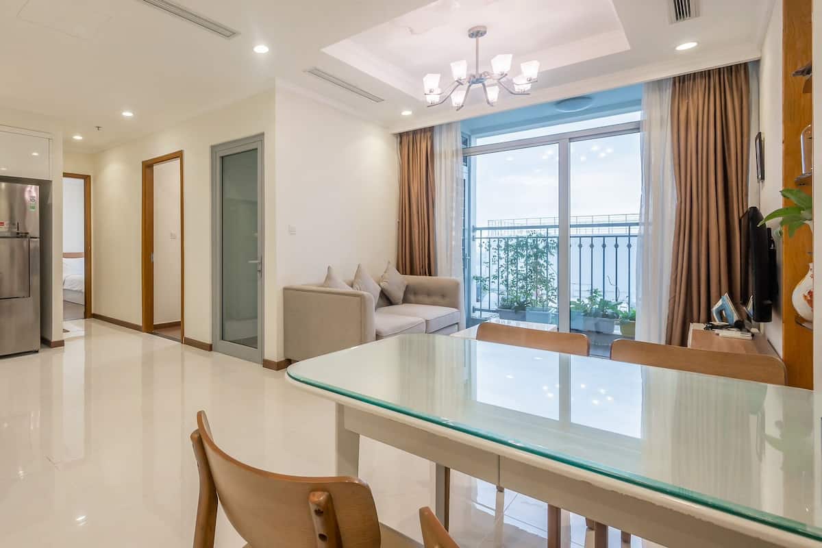A modern living room with a glass dining table, a sofa, and a balcony with a view.