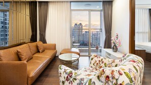 A modern living room with a brown leather sofa, a floral patterned armchair, a small round coffee table, and a view of a cityscape through large windows. - Landmark 81 Luxury - SaigonHomes (Ho Chi Minh City)