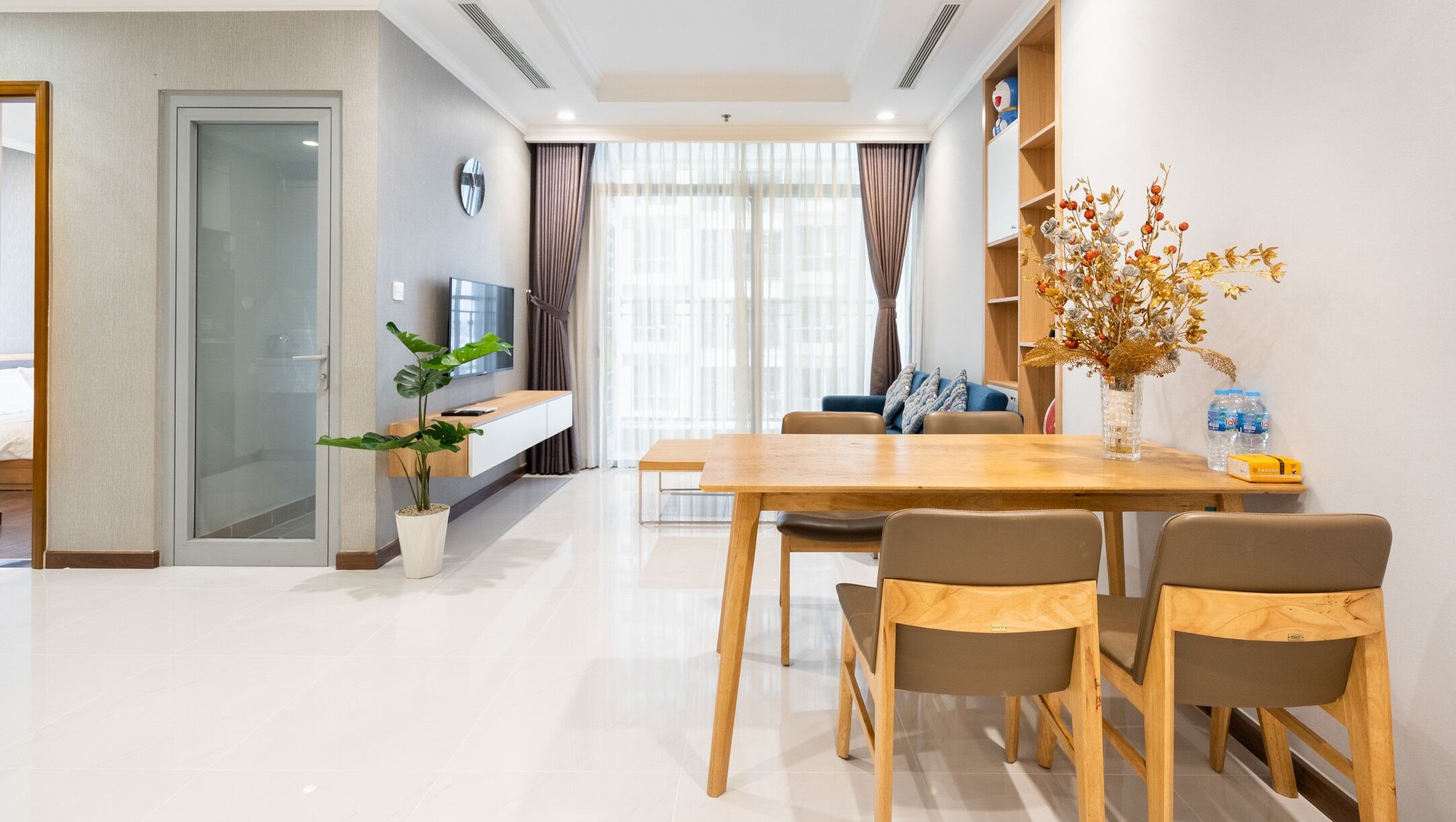 A modern hotel room with a dining area, a TV, a potted plant, and a decorative vase.