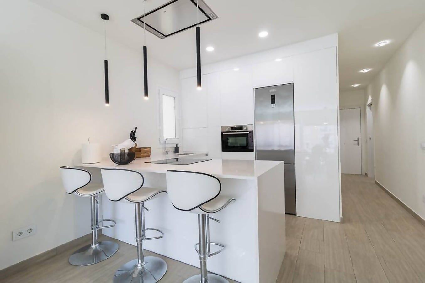 A modern kitchen with a central island, bar stools, a built-in oven, and a stainless steel refrigerator.
