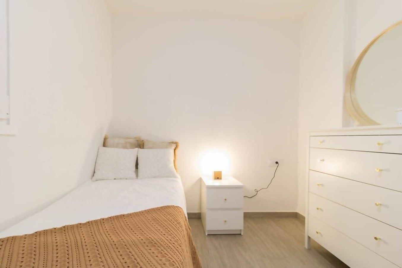 Une chambre à coucher comprenant un lit, une table de chevet, une commode et un miroir fixé au mur.