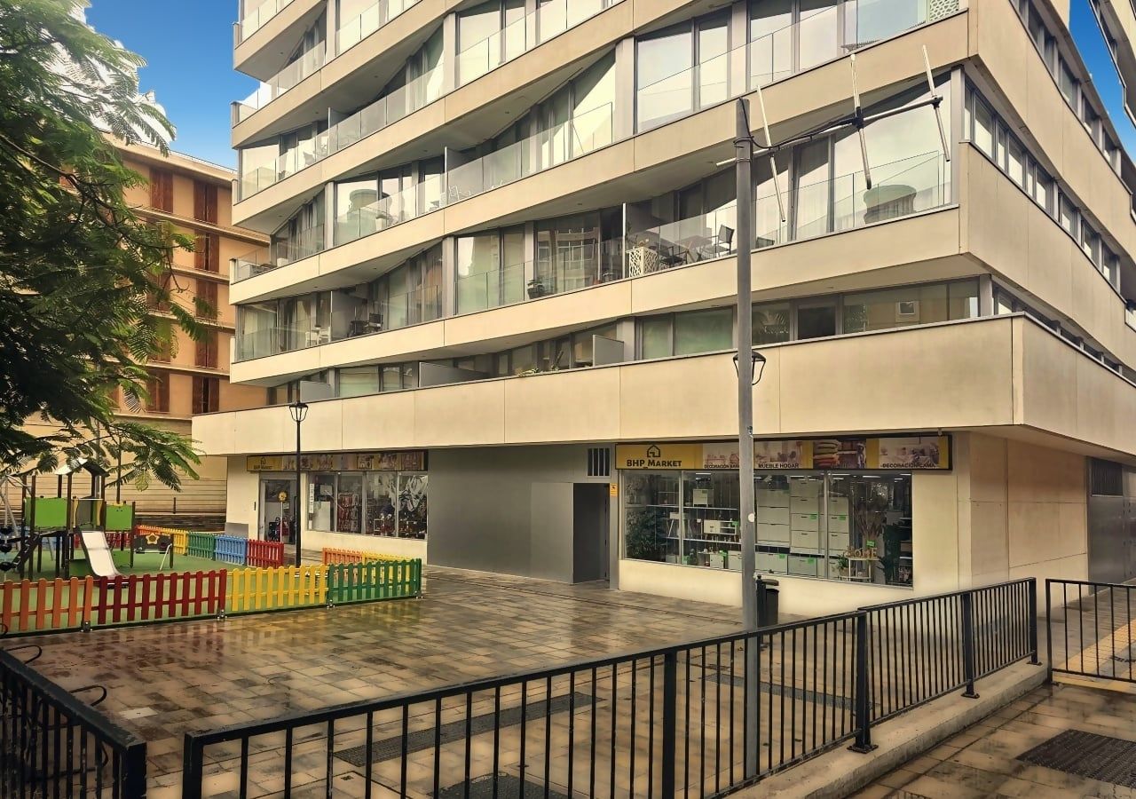 A multi-story building with a ground-level commercial space, a fenced outdoor area, and a pedestrian walkway.