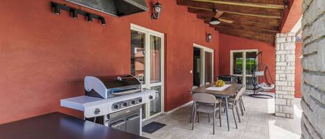 Una cocina al aire libre con una parrilla, una mesa y sillas.