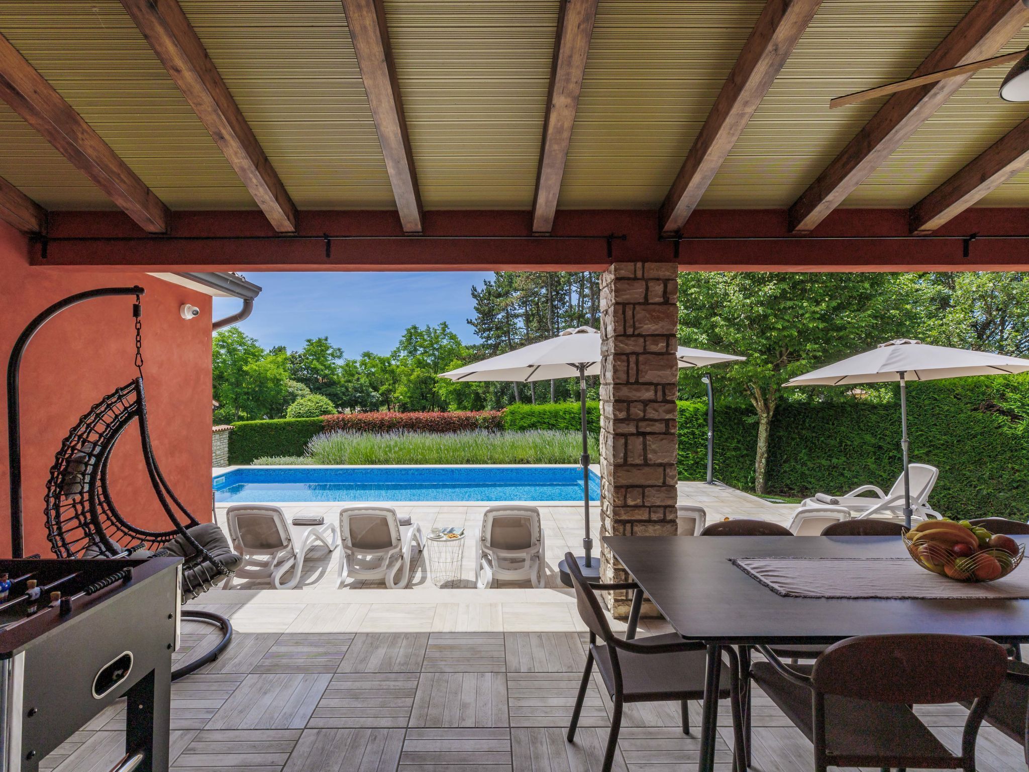 An outdoor patio with a pool, lounge chairs, a table with fruit, and a stone pillar.