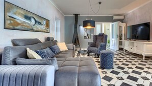 En stue med en grå sofa, mønstrede puder, en blå lænestol, et sofabord, en gulvlampe og et fjernsyn på et hvidt skab.