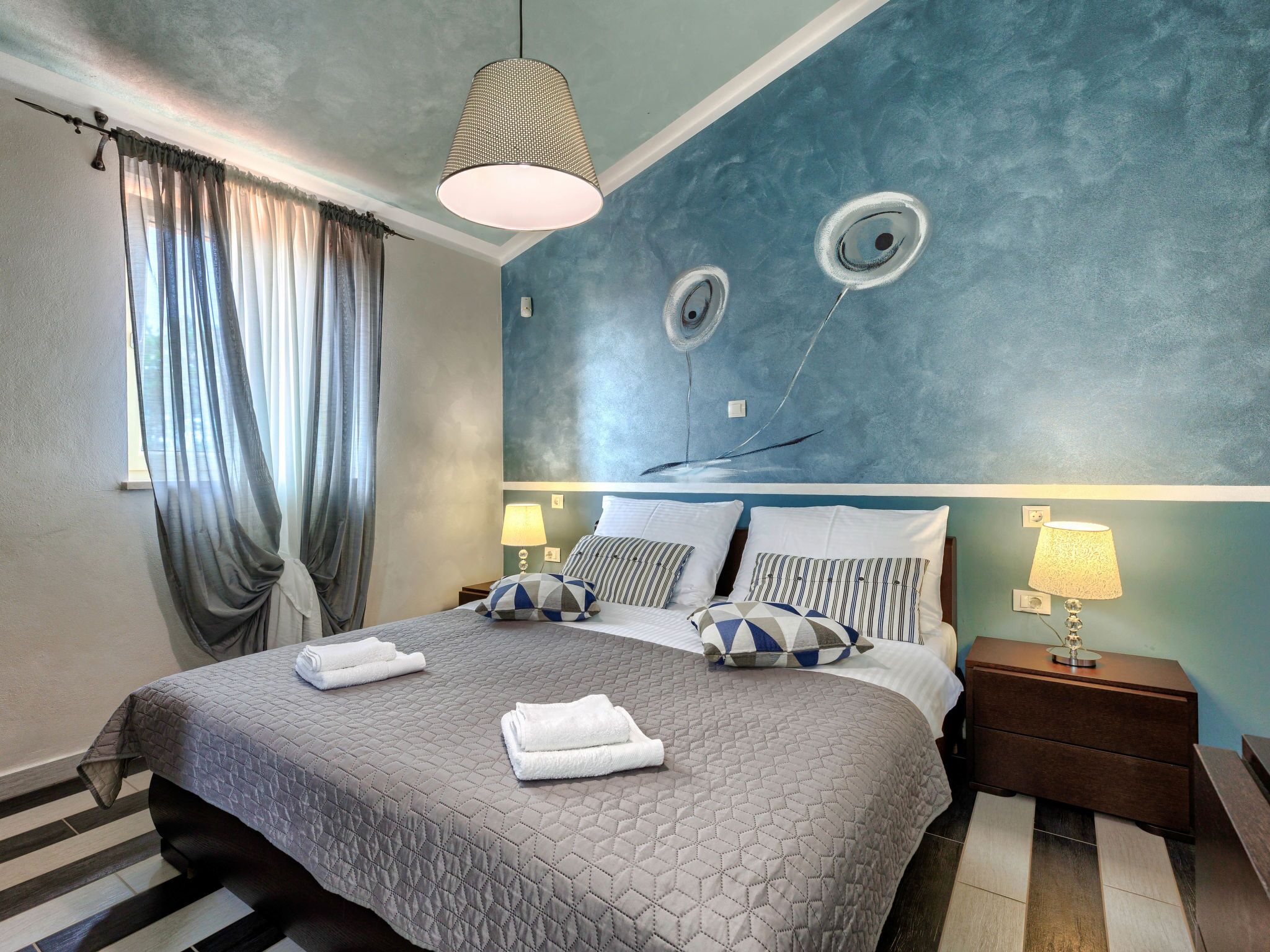 Une chambre d’hôtel avec un grand lit, deux tables de chevet, un luminaire suspendu et un mur orné de motifs circulaires.