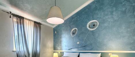 Une chambre d’hôtel avec un grand lit, deux tables de chevet, un luminaire suspendu et un mur orné de motifs circulaires.