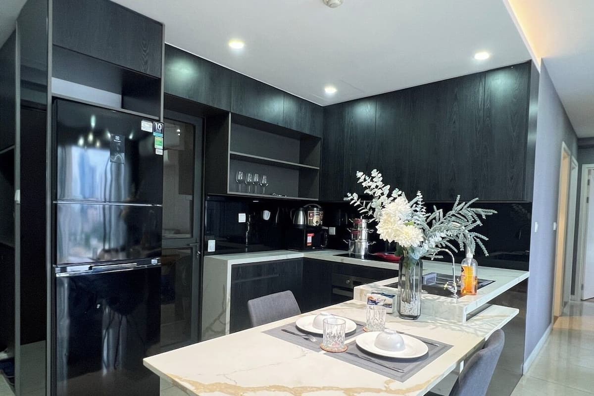 A modern kitchen with a built-in refrigerator, a dining table with a vase of flowers, and a coffee machine.