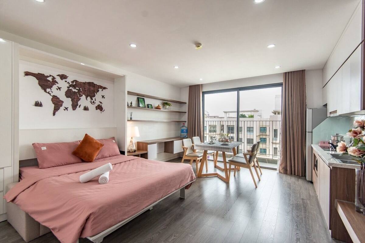 A modern hotel room with a bed, a desk, and a dining area. There is a world map on the wall and a view of the city through large windows.