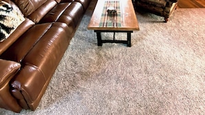 L’intérieur d’une cabane en rondins, avec un canapé en cuir, une table basse à motifs écossais et un fauteuil à motifs.