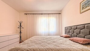 A bedroom with a bed, a coat rack, a window with curtains, and a painting on the wall. - Maldini by Interhome (Zadar/Sukošan)