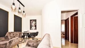 Een moderne woonkamer met een bank, stoelen, een eettafel en hanglampen.