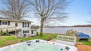 Un bain à remous dans un jardin, avec une maison et un lac en arrière-plan.