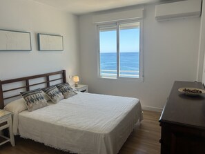 Et soveværelse med seng, natbord, lampe, et vindue med havudsigt og en trækommode.