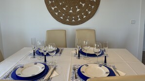 A dining table set for two with blue and white plates, clear glasses, and a decorative wall hanging above. - DELICIAS PLAYA, beachfront with parking included (Aguilas)