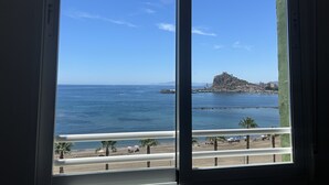 A coastal view through a window, featuring a beach, palm trees, a distant rocky hill, and a clear blue sky. - DELICIAS PLAYA, beachfront with parking included (Aguilas)