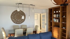 A modern living room with a blue sofa, a dining table with chairs, a wooden bookshelf, and pendant lights. - DELICIAS PLAYA, beachfront with parking included (Aguilas)