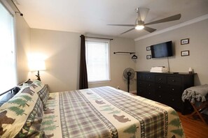 Un dormitorio con cama, ventilador de techo, televisión, cómoda y ventana con cortinas.