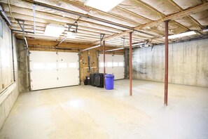 Un vaste sous-sol non aménagé, avec des poutres apparentes au plafond, des murs en béton et une grande porte de garage.