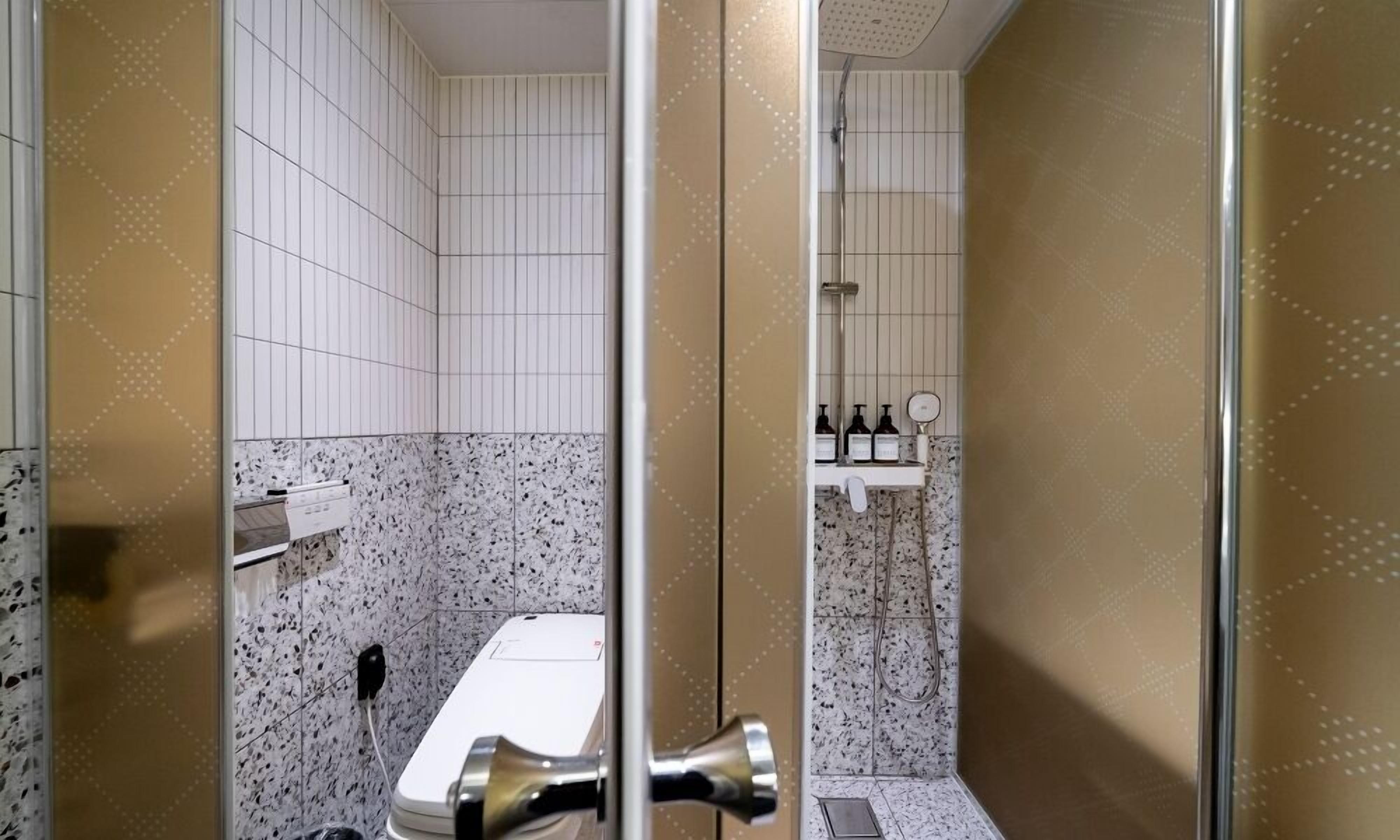 A bathroom with a white toilet, a shower area, and a sink with toiletries.