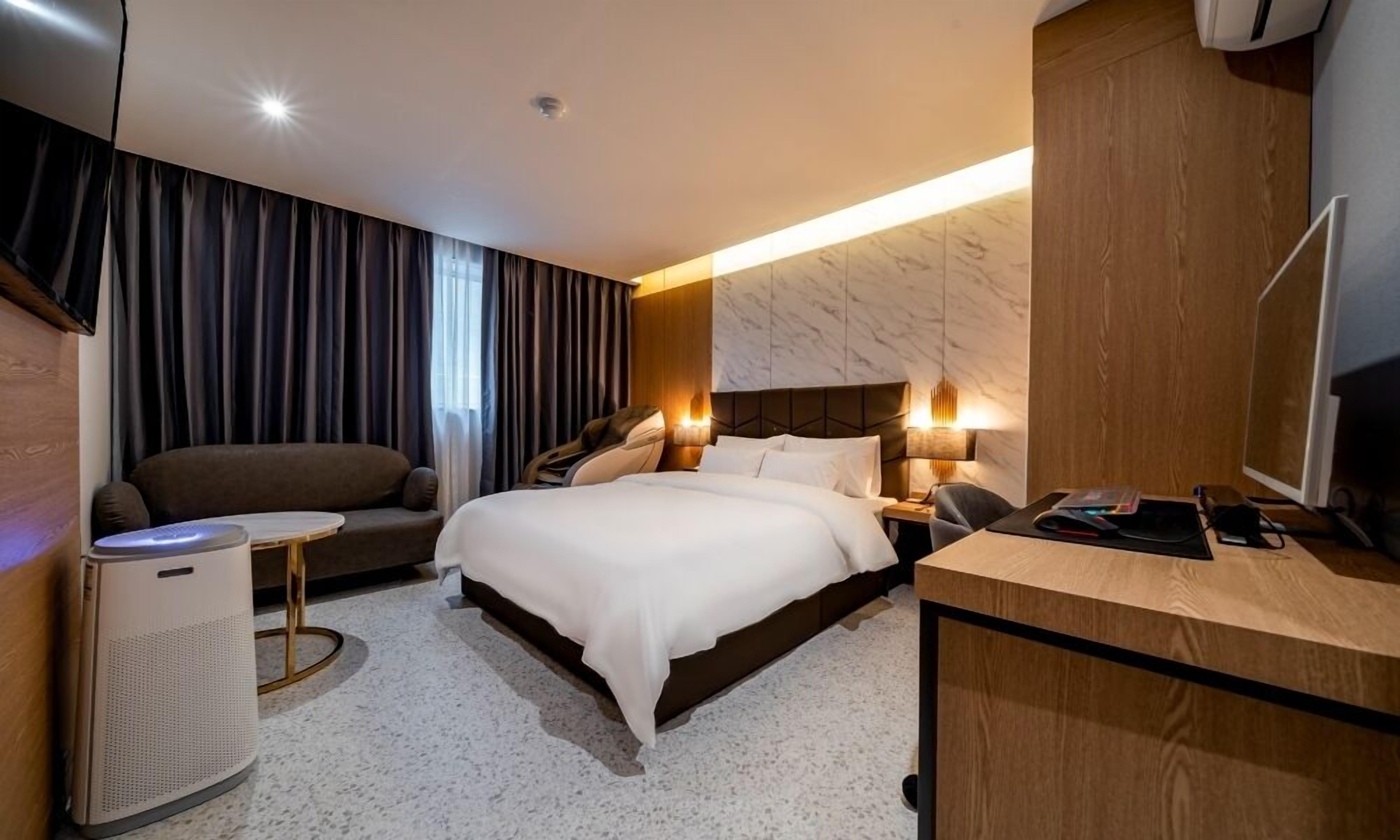 Ein modernes Hotelzimmer mit Bett, einer Couch, einem Schreibtisch und einem Massagesessel.
