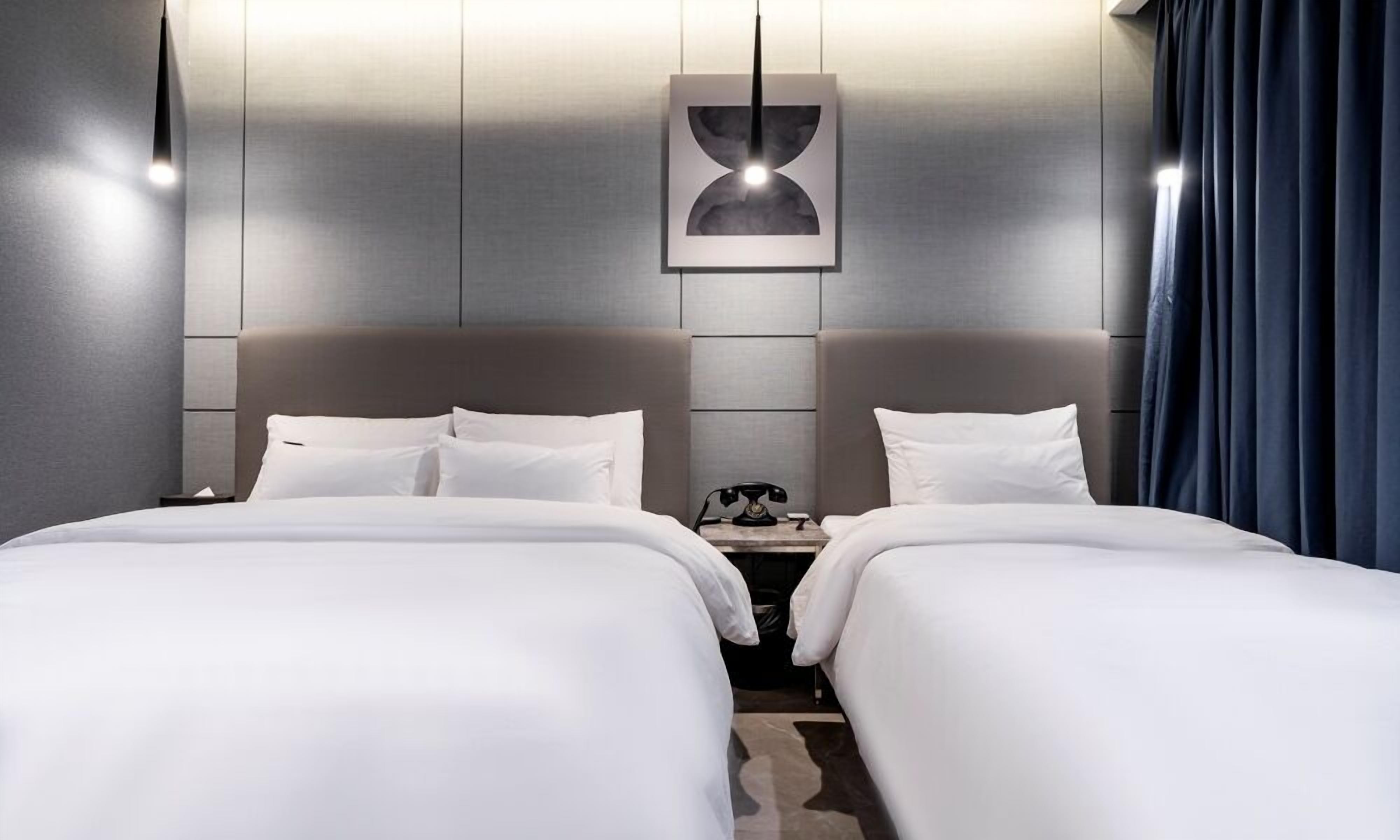 A hotel room with two beds, a nightstand with a telephone, and a framed picture on the wall.