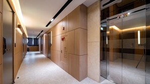 Een moderne hal met houten lambrisering, een glazen lift en een zichtbare brandmelder.