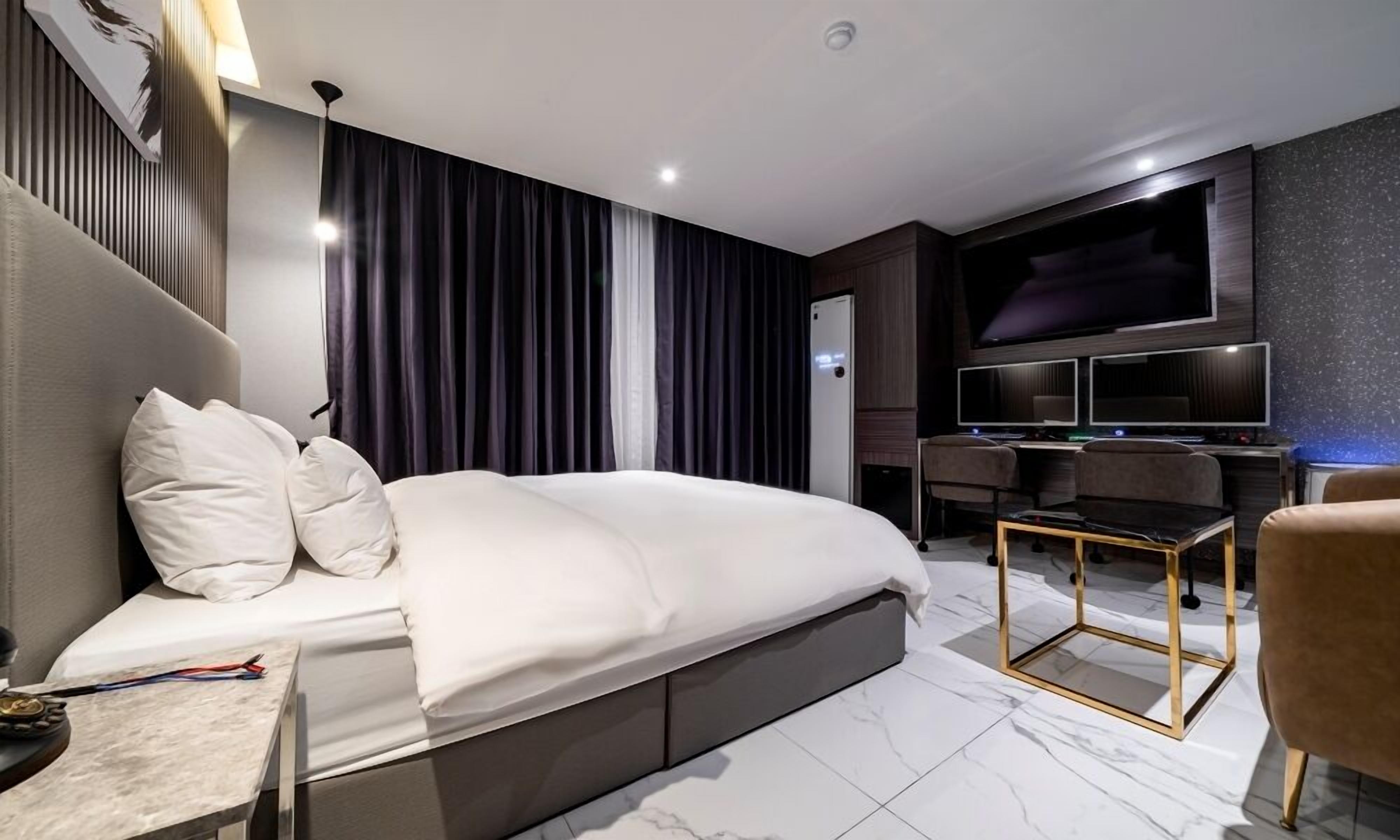 A modern hotel room with a large bed, a desk, a TV, and a seating area.