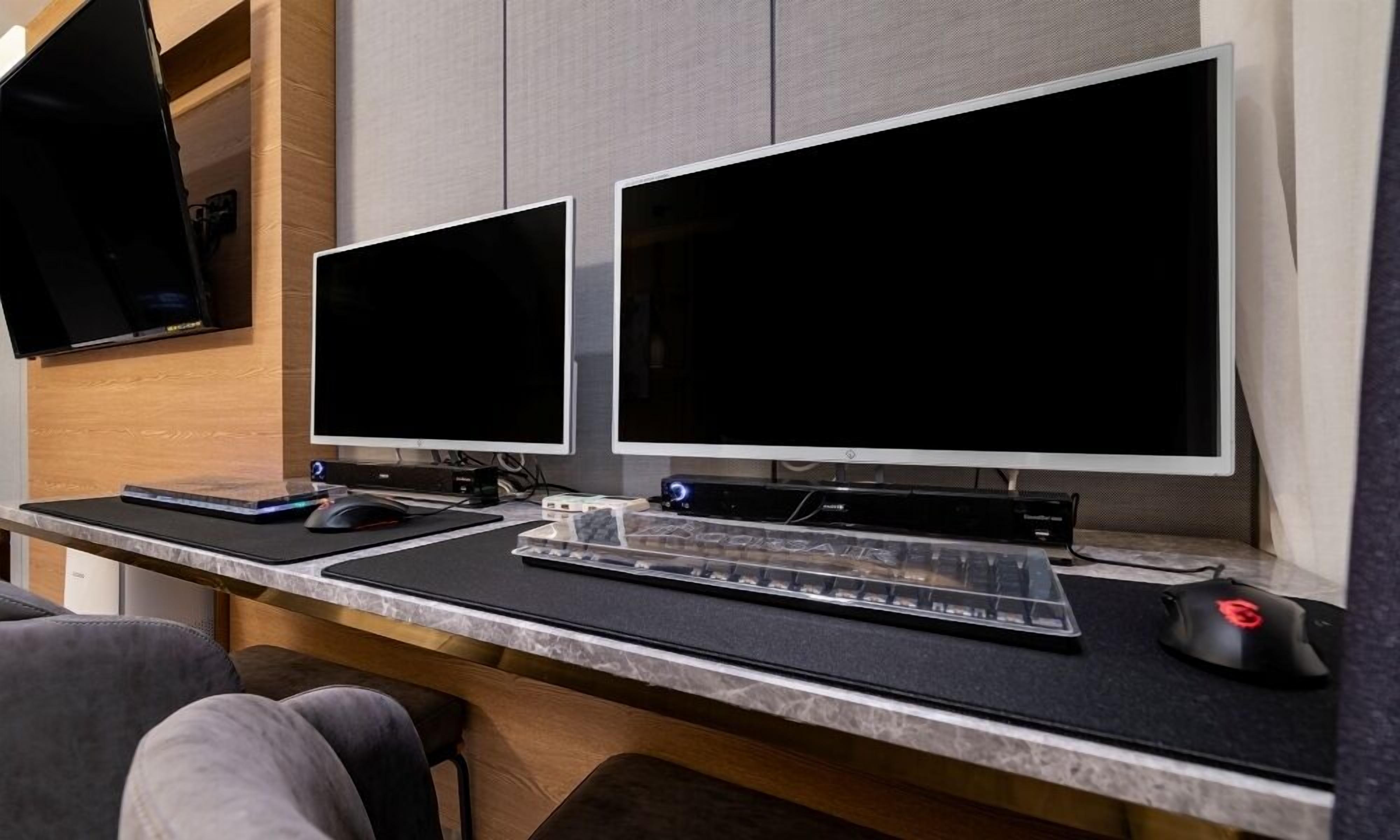 A dual-monitor workstation with a keyboard and mouse, set against a marble countertop in a modern office environment.