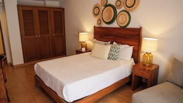 Un dormitorio con una cama de madera, dos mesitas de noche con lámparas, un armario y un panel decorativo con platos tejidos.