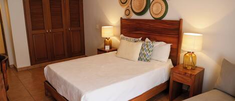 A bedroom with a wooden bed, two bedside tables with lamps, a wardrobe, and a wall decorated with woven plates.
